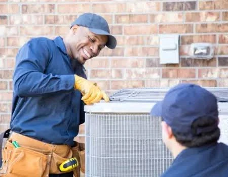 Two technicians working together on a residential outdoor air conditioning unit